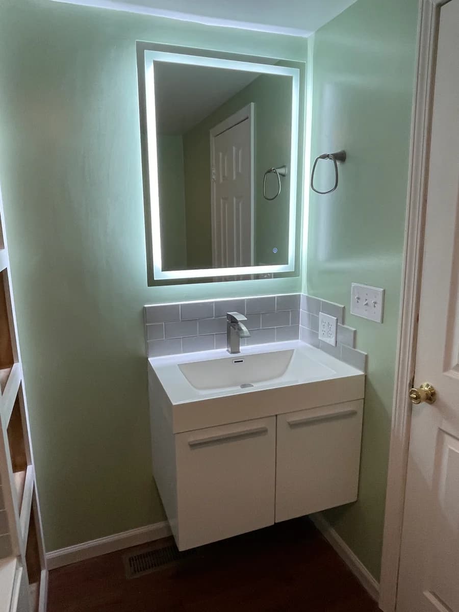 Completed vanity with illuminated mirror and gray tile backsplash